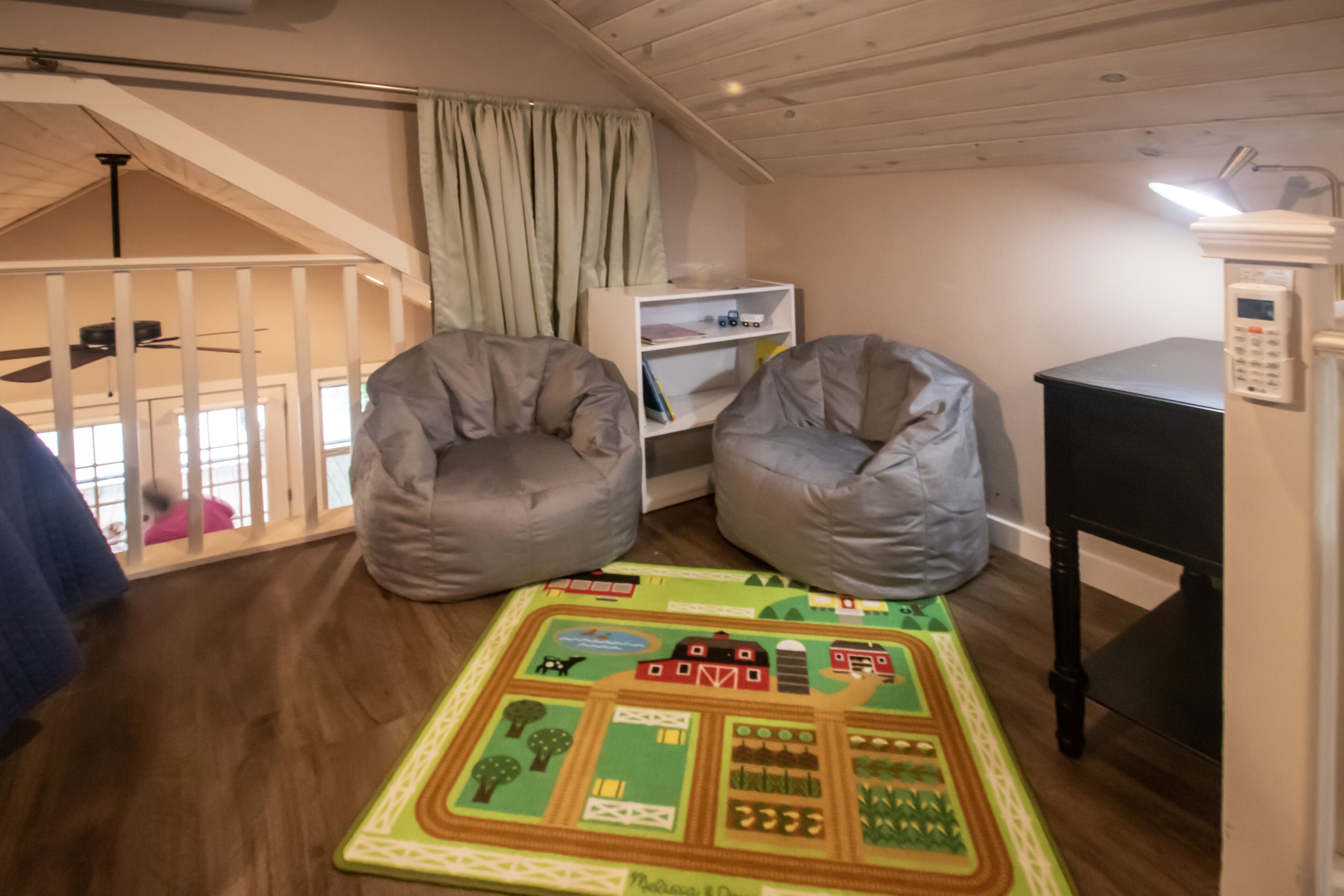 Une pièce avec un lit en mezzanine, deux fauteuils en forme de poire, une bibliothèque et un tapis de jeu.