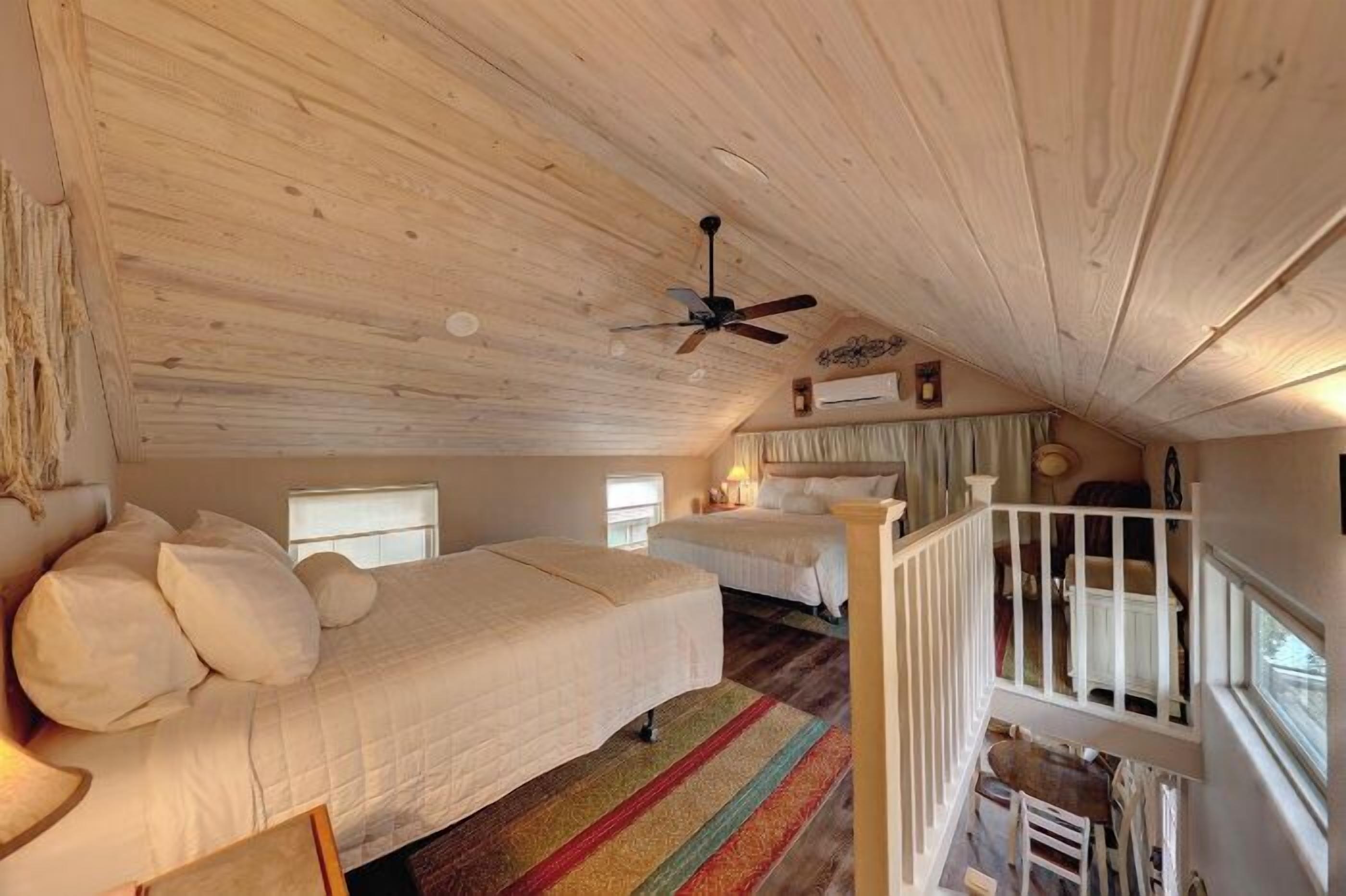 Een gezellig slaapkamer op zolder met twee bedden, een plafondventilator en een houten vloer.