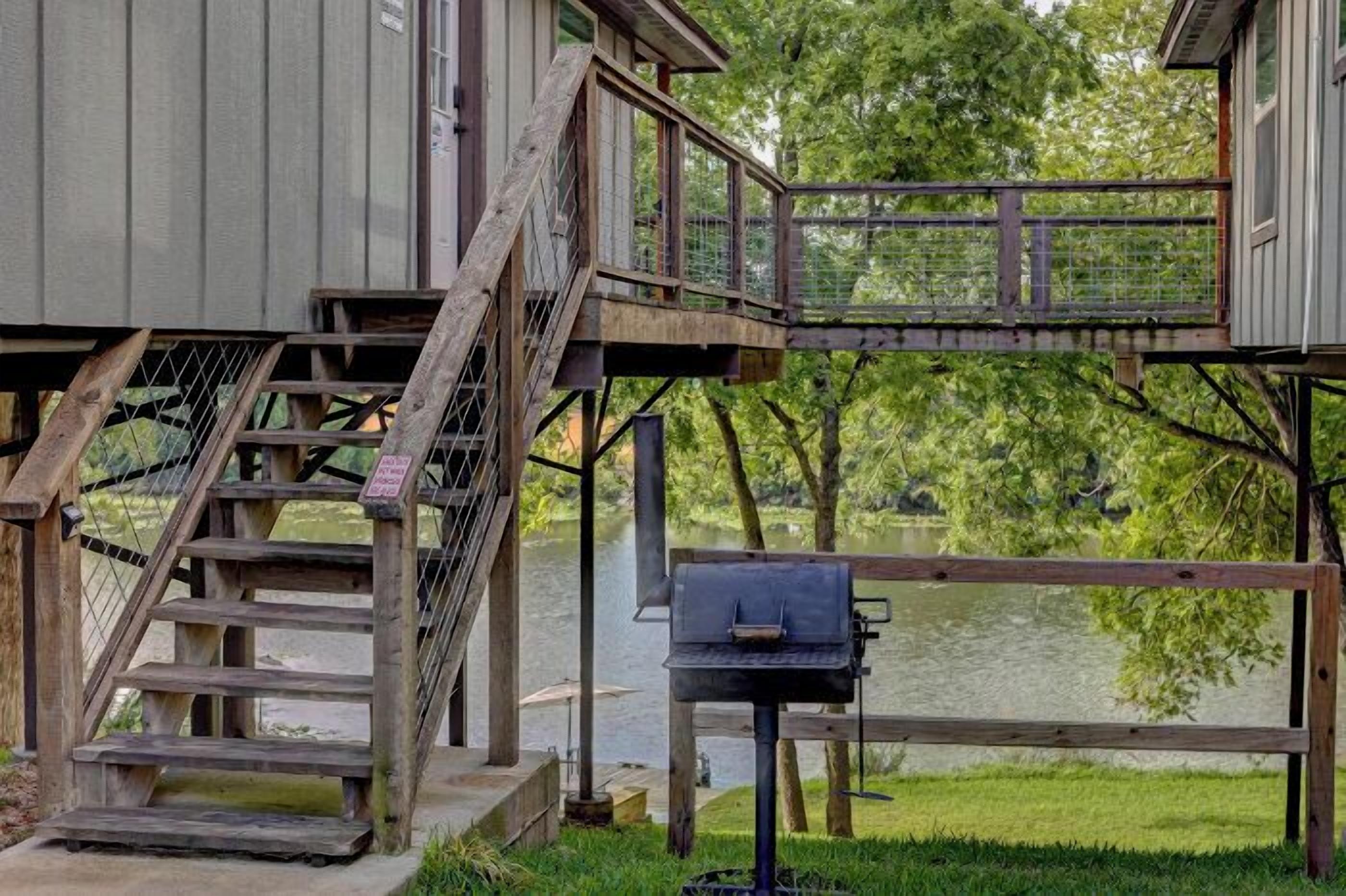 Une terrasse en bois avec un barbecue, un escalier et une vue sur un lac.