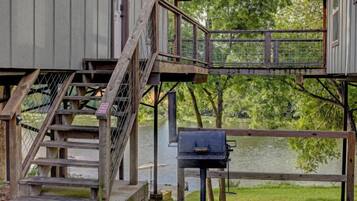 Une terrasse en bois avec un barbecue, un escalier et une vue sur un lac.