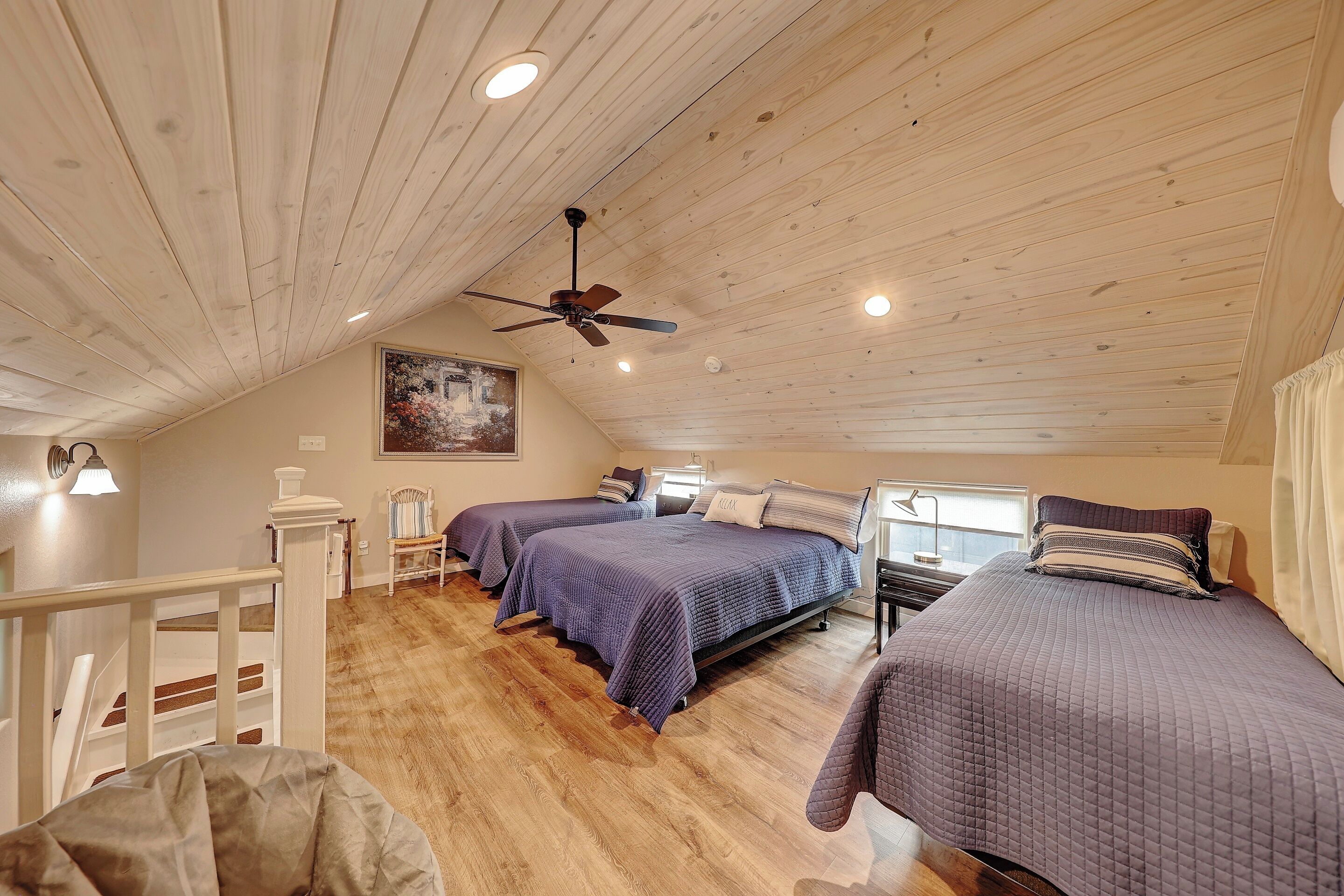 Ein Schlafzimmer mit zwei Betten, Holzboden, Deckenventilator und einem Gemälde an der Wand.