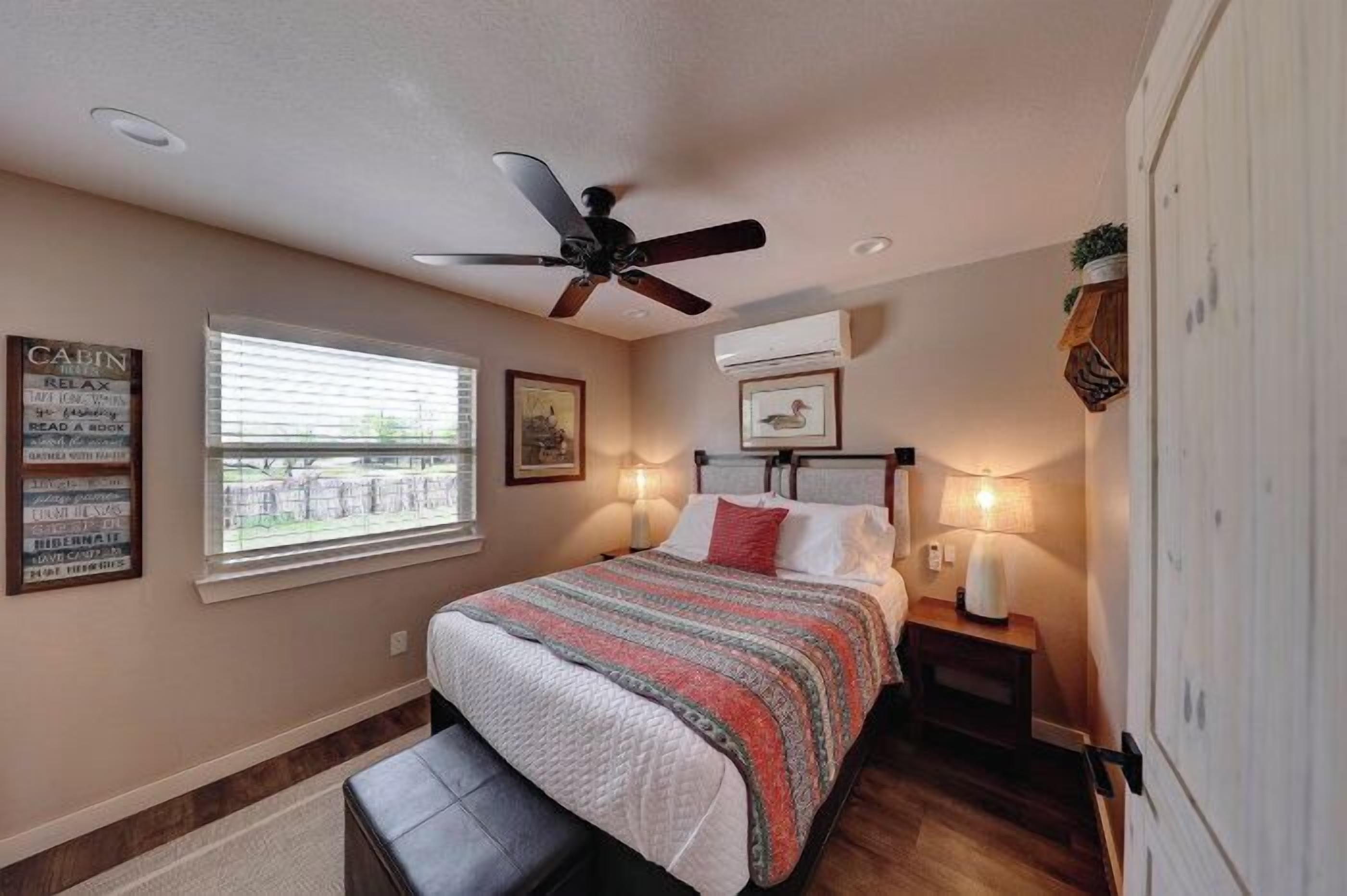 Un dormitorio con una cama, ventilador de techo, ventana con persianas y aire acondicionado instalado en la pared.