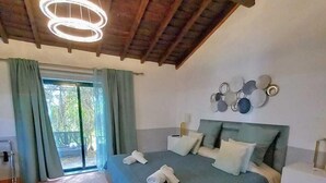 A bedroom with a bed, a nightstand, a wall-mounted light fixture, and a view of the outdoors through a window. - Agroturismo Herdade Fonte Ferreira (Avis)