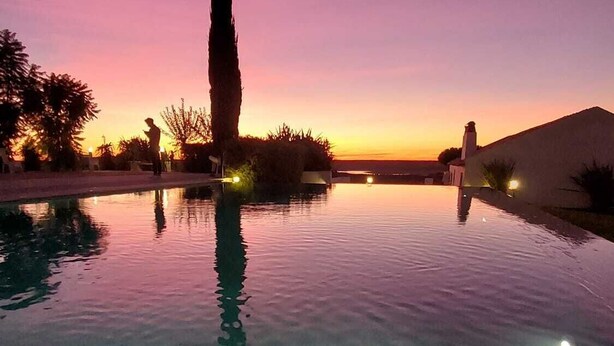 An infinity pool with a clear view of the sunset, a tall tree, and a building in the background. - Agroturismo Herdade Fonte Ferreira (Avis)