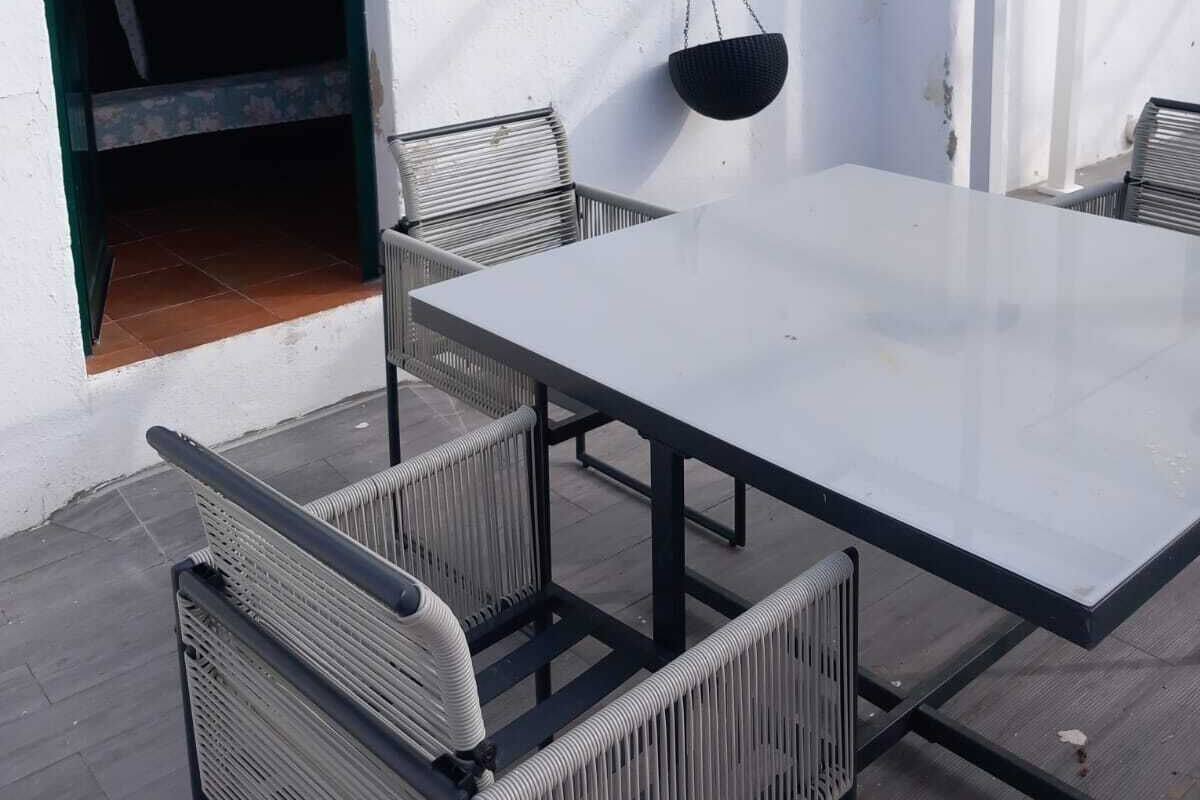 An outdoor patio with a table and chairs, a hanging basket, and a white wall.