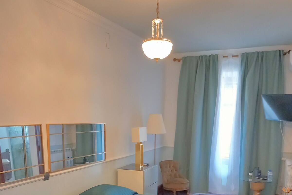 A hotel room with two beds, a chair, a lamp, a TV, and a window with curtains.