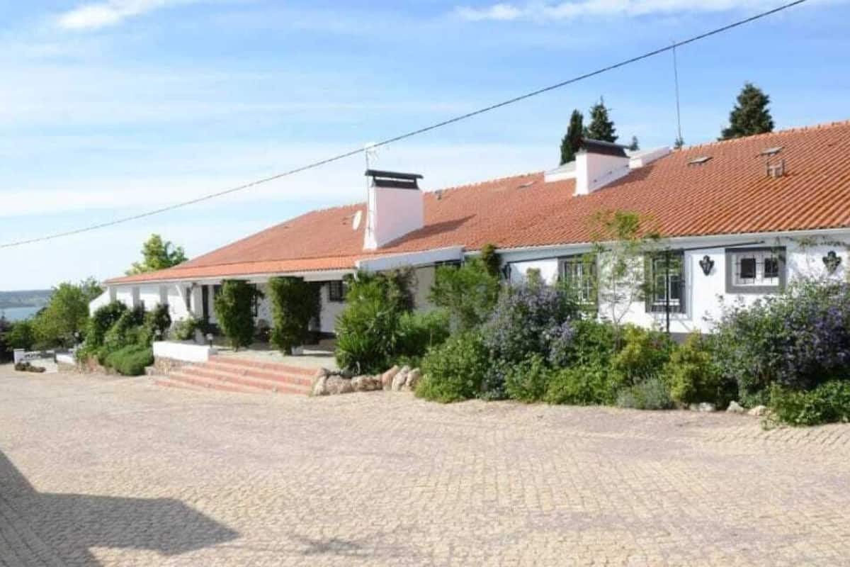 A two-story house with a red-tiled roof, a white exterior, and a paved driveway leading to a set of steps.