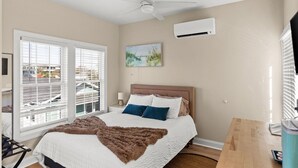 A bedroom with a bed, a ceiling fan, an air conditioning unit, a window with blinds, and a painting on the wall. - Hanby Hideaway~ Cottages @ Kure ~ Beach, Fishing, Pool, Walk to Pier (Kure Beach)