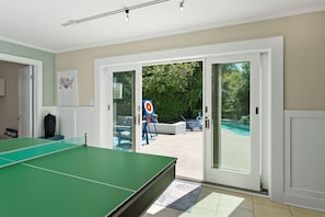 Una habitación con mesa de ping pong, una puerta que da al exterior y vista a una piscina.