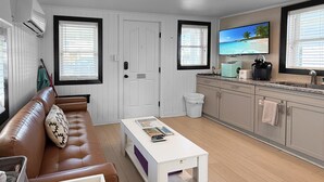Una sala moderna con un sofá de cuero marrón, una mesa de centro blanca y una cocina integrada con horno y fregadero.