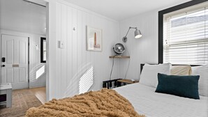 Un dormitorio con cama, mesita de noche, lámpara, ventilador y ventana con persianas.