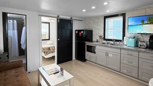 A modern kitchen with a refrigerator, stove, and sink. There is a dining area with a table and chairs, and a living room with a sofa and a coffee table. - Wilmington Beach Bungalow~ Kure Beach, Fishing, Pool, Walk to Pier (Kure Beach)