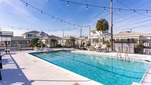 A rectangular swimming pool with a 6 ft depth marker, surrounded by lounge chairs and umbrellas, under string lights. - Wilmington Beach Bungalow~ Kure Beach, Fishing, Pool, Walk to Pier (Kure Beach)