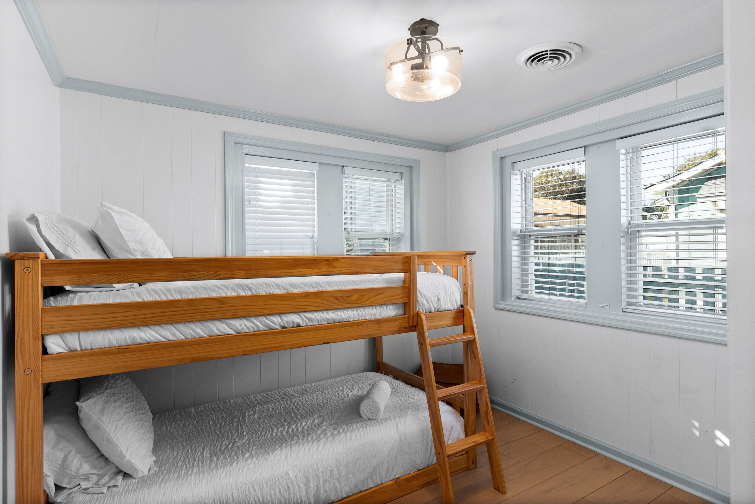 A bunk bed room with white walls, wooden flooring, and a window with blinds.