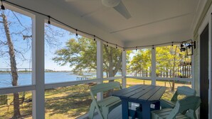 Un porche cubierto con una mesa y sillas, con vista a un lago rodeado de árboles y un muelle.
