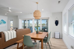 A modern living room with a wooden dining table, green chairs, a brown leather sofa, and a ceiling fan.