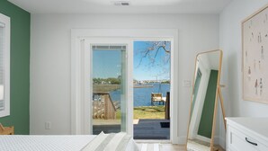 Un dormitorio con cama, un espejo grande, vista a una terraza y agua, y una pared verde.