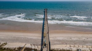 Un muelle se adentra en el océano, con una playa arenosa al frente.