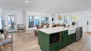 Una cocina moderna con una isla verde, un comedor con vistas y una sala de estar con sofá y sillones.