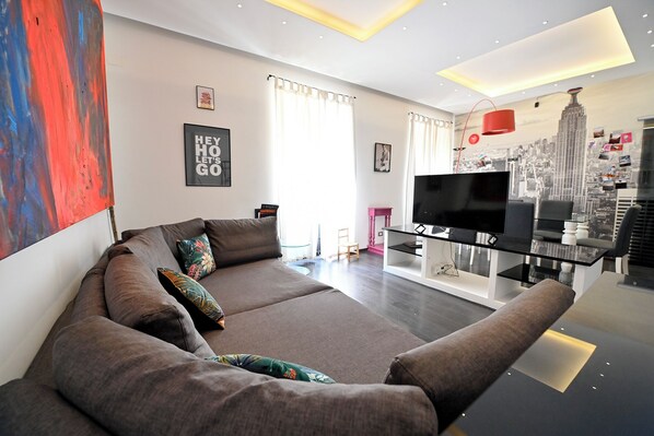 A modern living room with a sofa, a flat-screen TV, and a cityscape mural on the wall. - Luxury apt Villa Borghese (Roma)