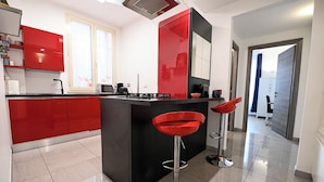 Une cuisine moderne avec des meubles rouges, un îlot central noir et deux tabourets de bar rouges.