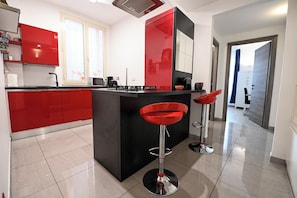 A modern kitchen with red cabinets, a black island, and two red bar stools. - Luxury apt Villa Borghese (Roma)