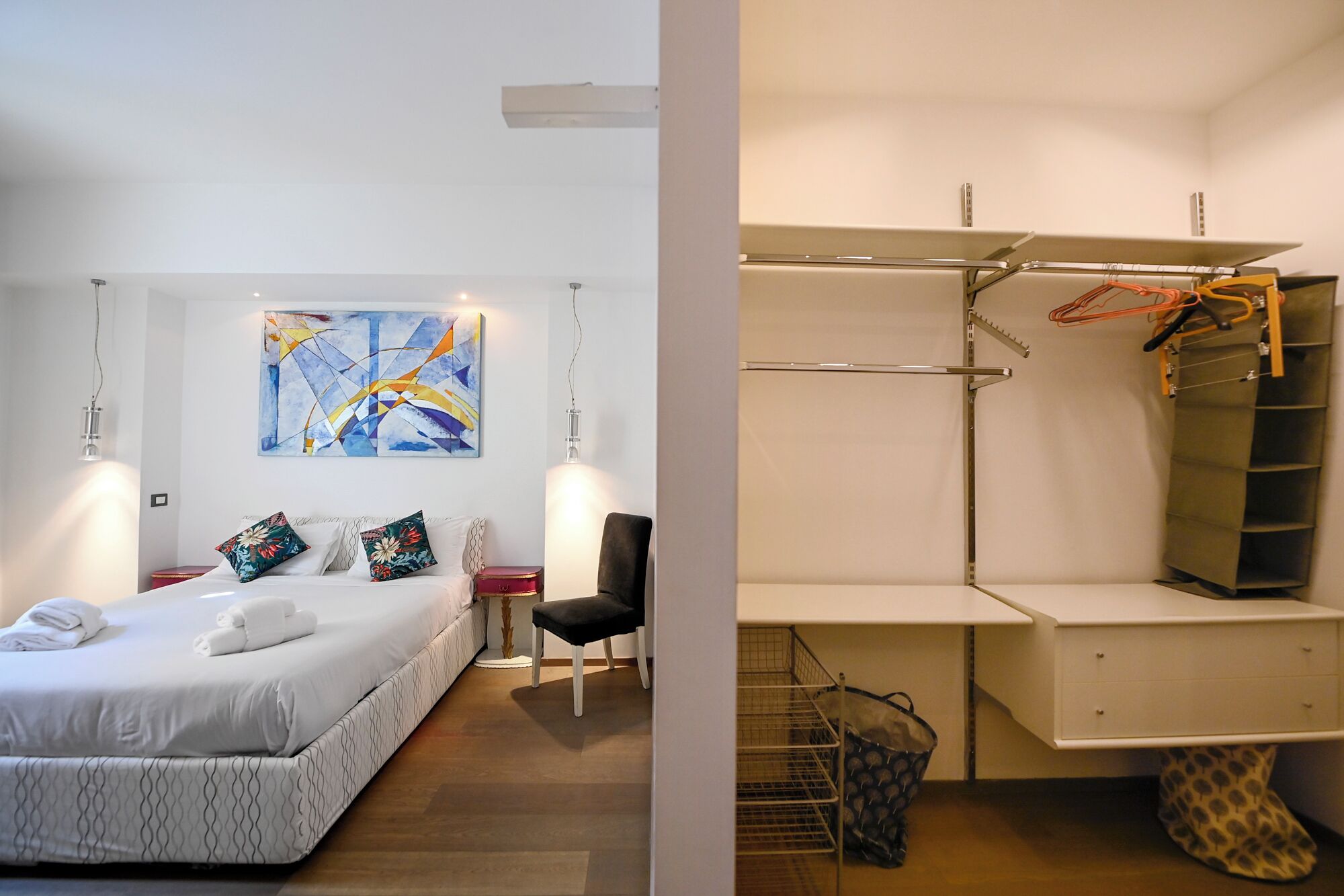 A modern bedroom with a bed, bedside tables, a chair, and a painting on the wall.