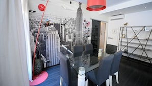 Une salle de réunion moderne avec une table en verre, des chaises noires, un luminaire suspendu rouge et une fresque représentant un paysage urbain sur le mur.