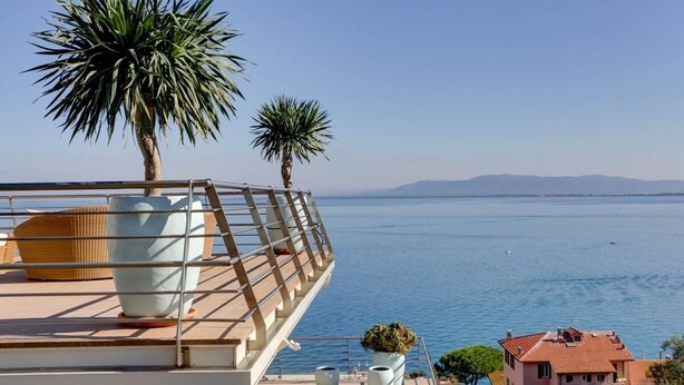 Ein Balkon mit Meerblick, zwei Palmen und ein Gebäude im Hintergrund.