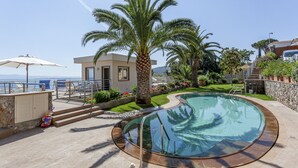 Ein Pool mit gewölbter Kante, umgeben von Palmen und einem kleinen Gebäude.