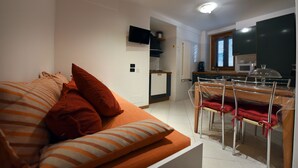 A compact living space with a sofa, a dining table with chairs, a kitchen area, and a flat-screen TV mounted on the wall. - Vista sui sassi civico 16 (Matera)