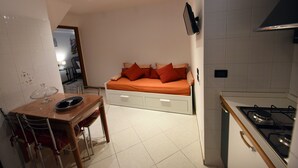 A compact kitchen with a dining area and a bed with orange bedding. - Vista sui sassi civico 16 (Matera)