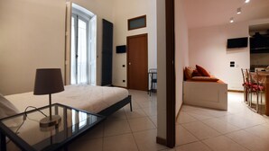 A modern bedroom with a glass bedside table, a bed, a desk, and a seating area with a sofa. - Vista sui sassi civico 16 (Matera)