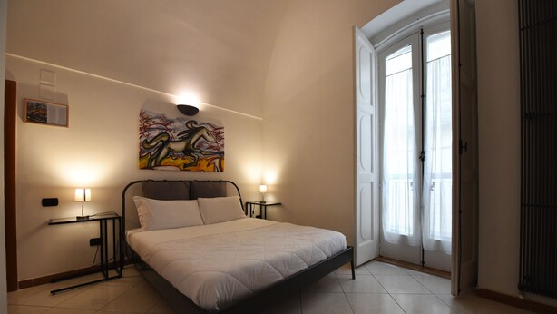 A bedroom with a bed, two bedside tables, a wall-mounted painting, and a door with curtains. - Vista sui sassi civico 16 (Matera)
