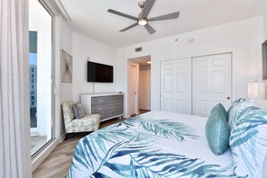 A bedroom with a large bed, a ceiling fan, a TV, a dresser, and a door leading to another room. - Coastal Serenity! Updated Condo at The Palms of Destin 🌴 (Destin)