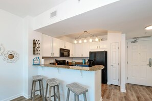 A kitchen with white cabinets, a black refrigerator, a microwave, and a bar area with stools. - Coastal Serenity! Updated Condo at The Palms of Destin 🌴 (Destin)