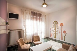 A room with a large window, a radiator, two chairs, a table, and a wall with floral decals.