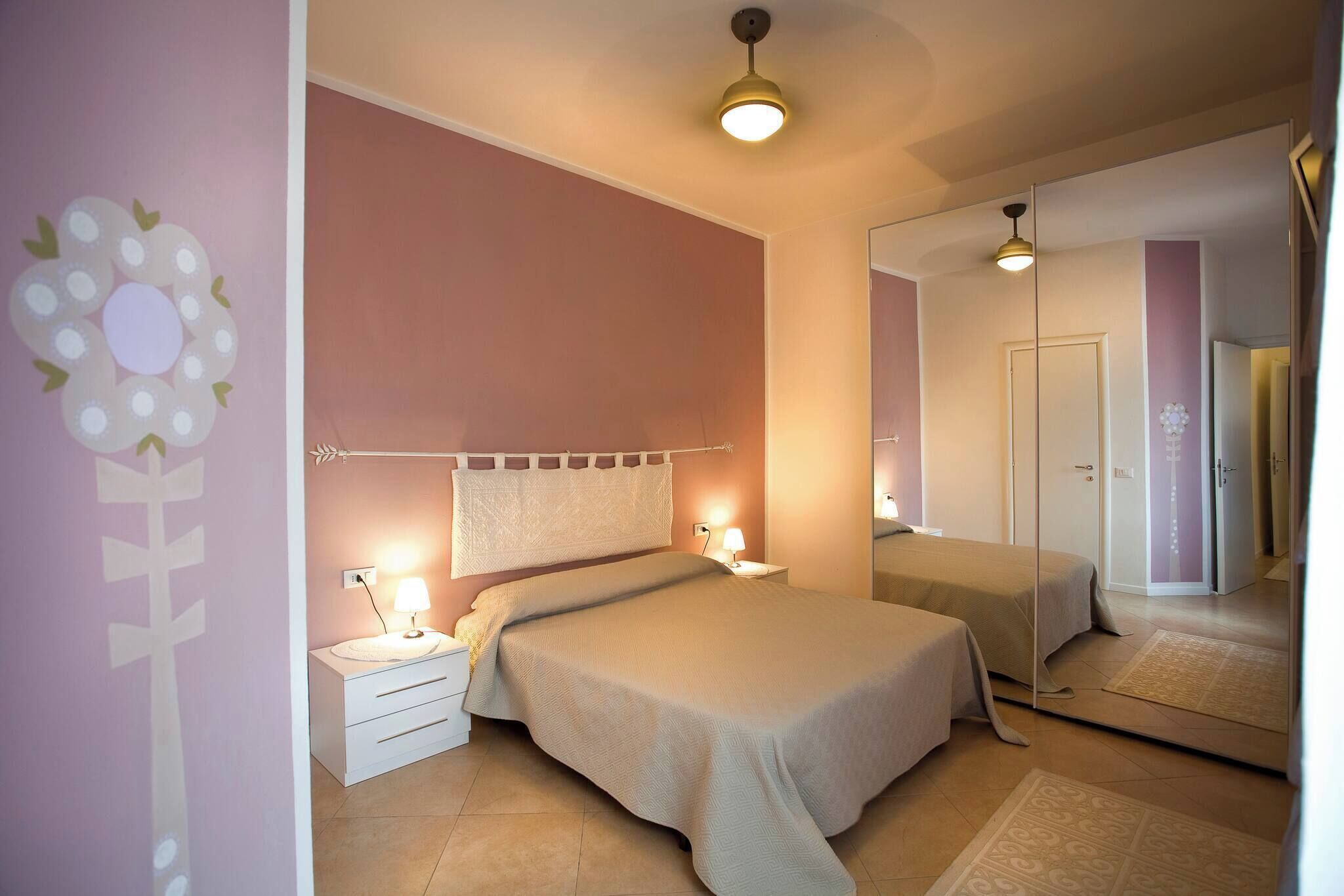 A bedroom with a bed, bedside tables, a mirror, and a wall decoration.