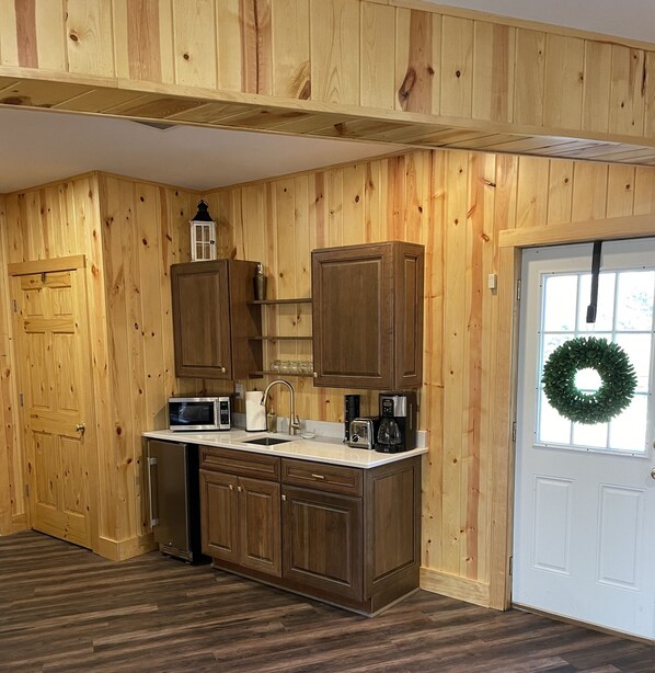 Une cuisine avec des murs lambrés en bois, une porte blanche et une fenêtre décorée d’une guirlande.