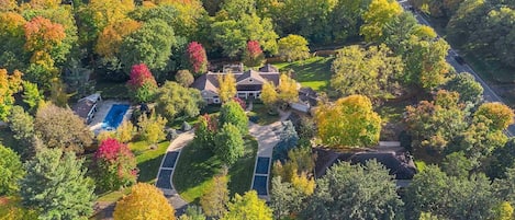 An aerial view of a residential property with a swimming pool, a driveway, and a large house surrounded by trees.