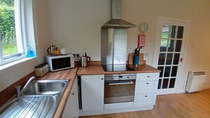 A compact kitchen with a sink, microwave, toaster, kettle, and a stove.