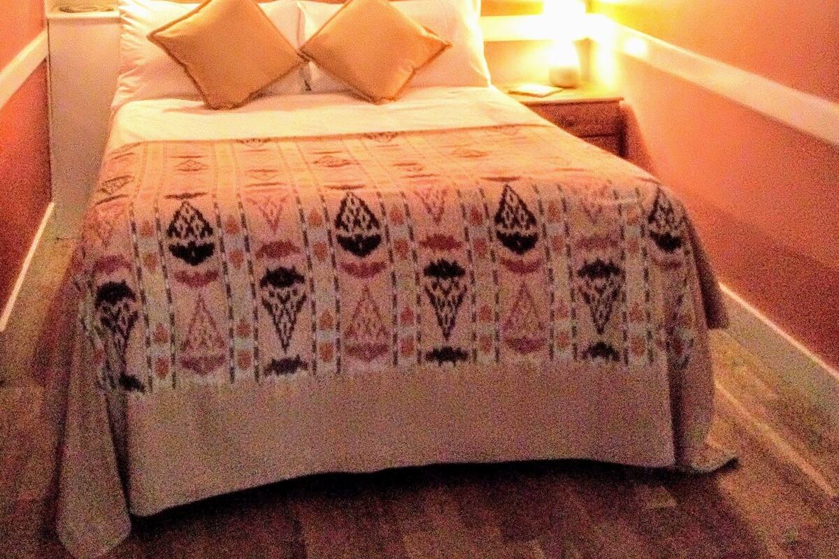 A hotel room with a bed, a nightstand, a bookshelf, and a framed picture on the wall.