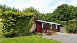 A small, single-story building with a red door and windows, surrounded by lush greenery and a well-maintained lawn.