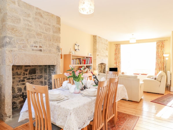 A cozy living room with a fireplace, a dining area with a table set for four, and a comfortable seating area with a sofa. - Southview Amble (Morpeth)
