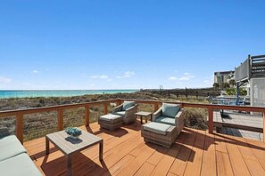 Eine Holzterrasse mit Gartenmöbeln mit Blick auf einen Strand und den Ozean.