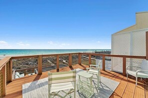 Une terrasse en bois, agréée de mobilier d’extérieur, donnant sur une plage.