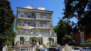 Un edificio de varios pisos con balcones, un acceso con reja y automóviles estacionados.