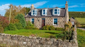 A stone house with a sloped roof, dormer windows, and a stone wall in the foreground. - Wynford Holiday Cottages (Aberdeen)