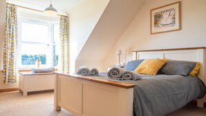 A bedroom with a bed, a bedside table, a lamp, and a window with curtains. - Wynford Holiday Cottages (Aberdeen)