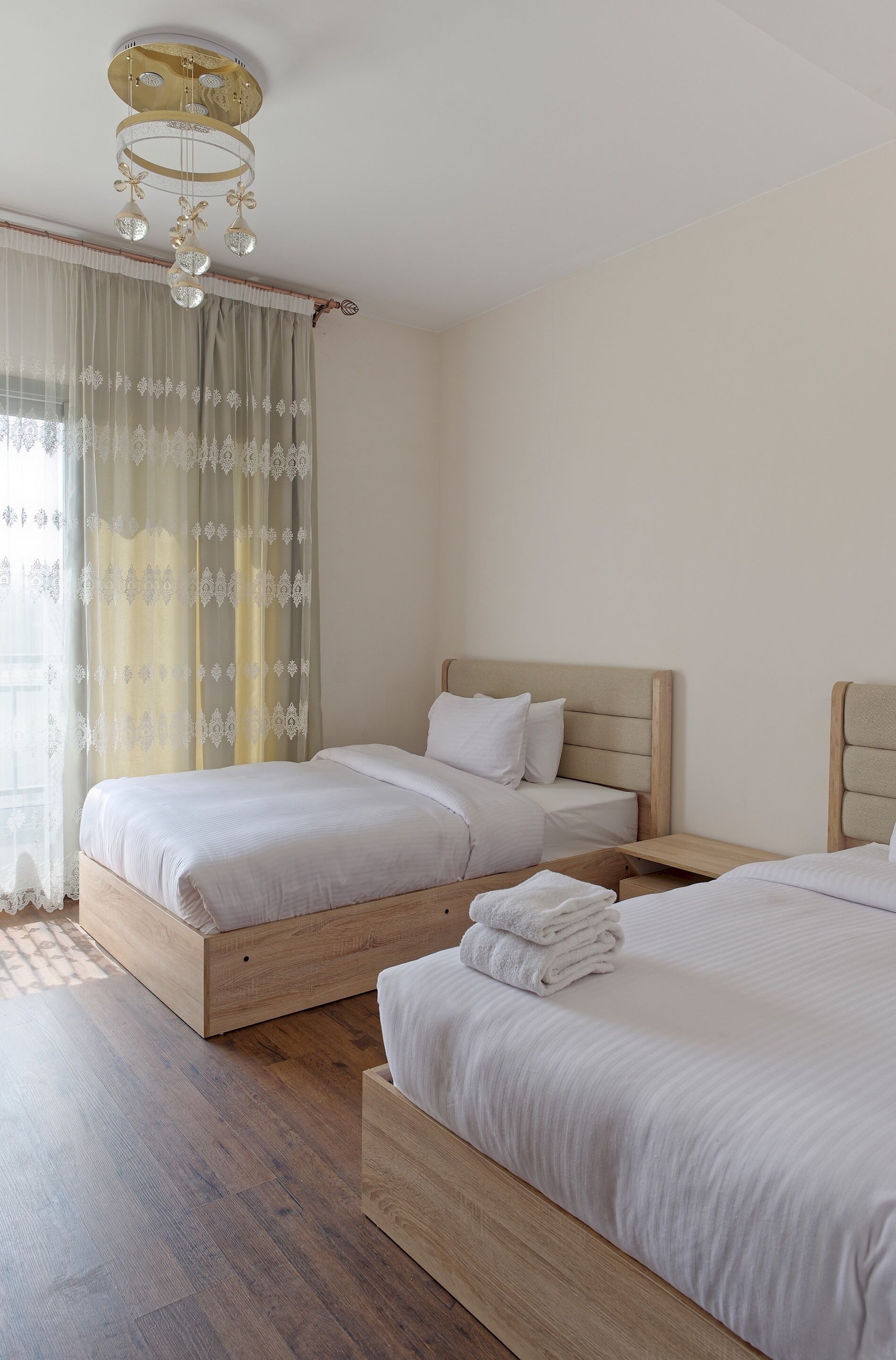 A hotel room with two wooden beds, a chandelier, and sheer curtains.